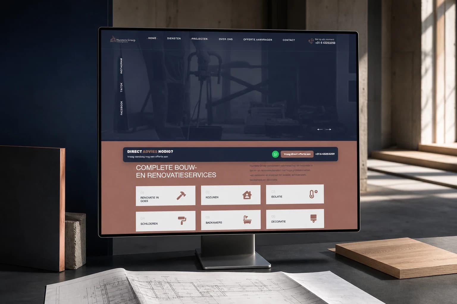 Hunters Groep website op een breed beeldscherm in een architecturale studio met bouwtekeningen en materiaalstalen.